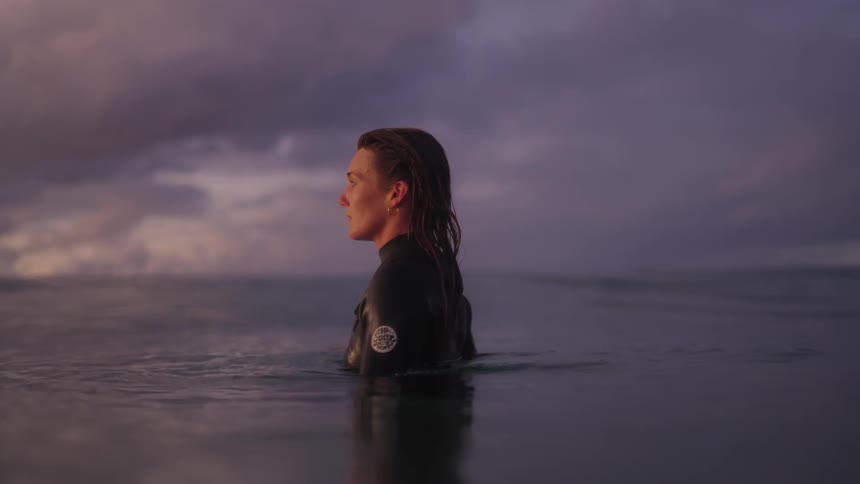 A woman in a surf suit inside the sea watching the sunrise over the ocean