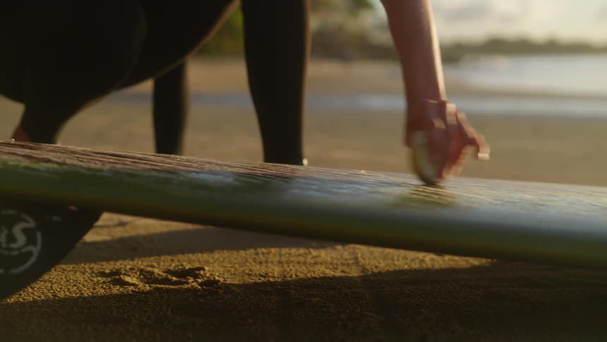 Hands of a woman applying wax to a surfboard on the beach
