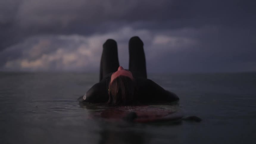 Woman floats over a surfboard in the ocean at evening