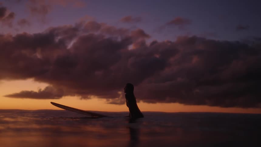 Young attractive girl waits alone for a wave at sunset