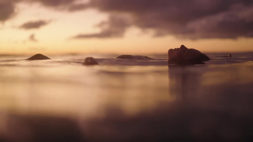 A young attractive woman relaxing & contemplating in the ocean at sunset