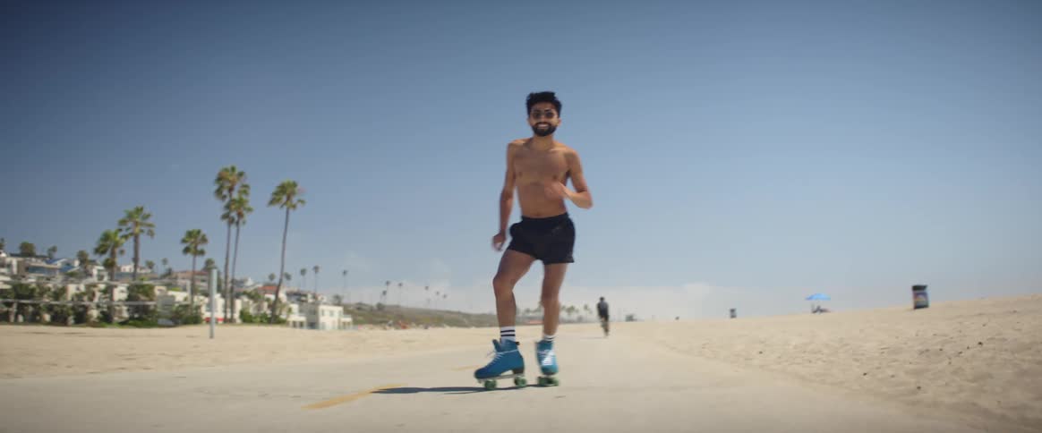 A man roller skating and dancing on the sidewalk of a beach