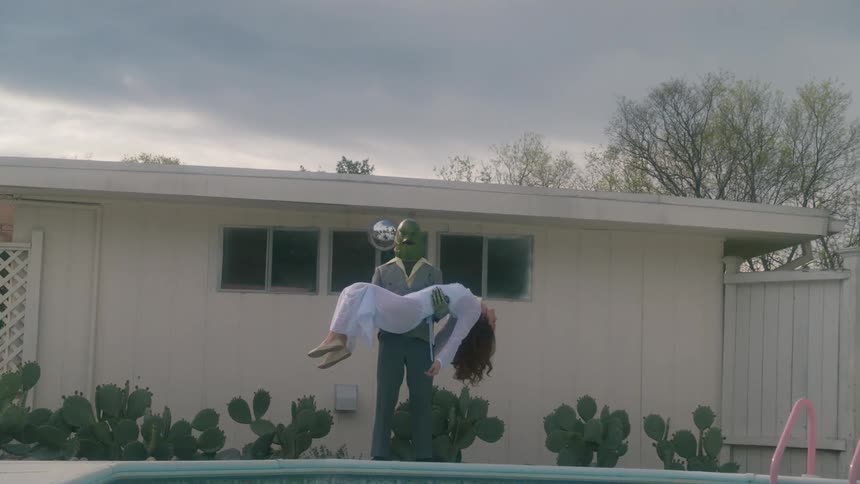 A man wearing a mask holding a woman in his arms facing a swimming pool