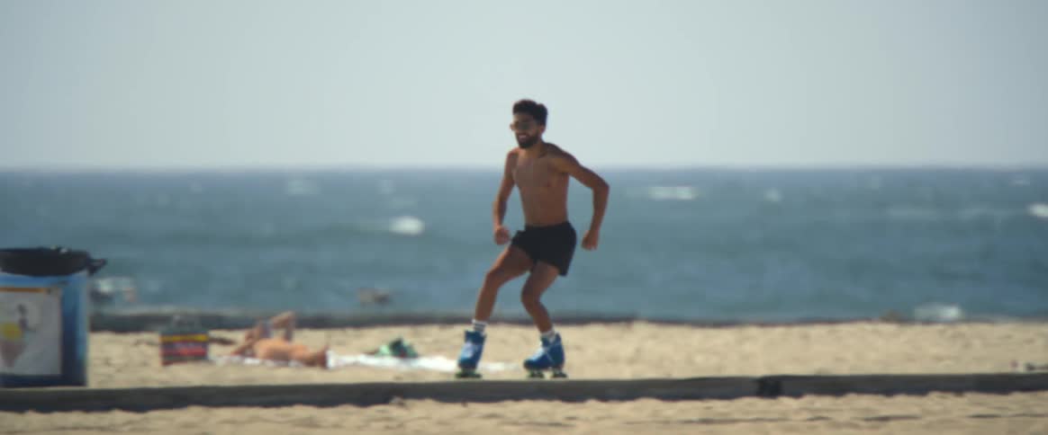 Shirtless man rollerskating on the beachside sidewalk