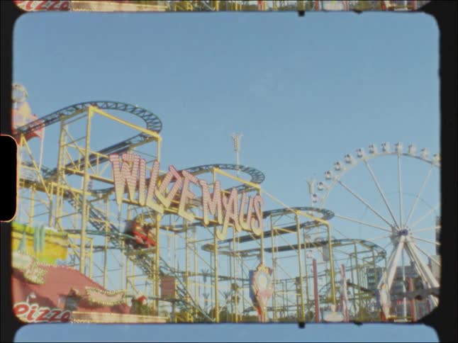 Roller coaster cars move along tracks as people pass through amusement park
