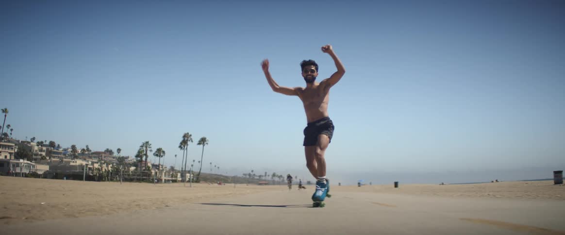 A shirtless man skating on a path near the beach at midday