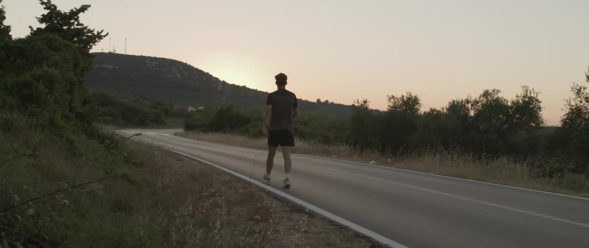 A man walks on a deserted road at sunset