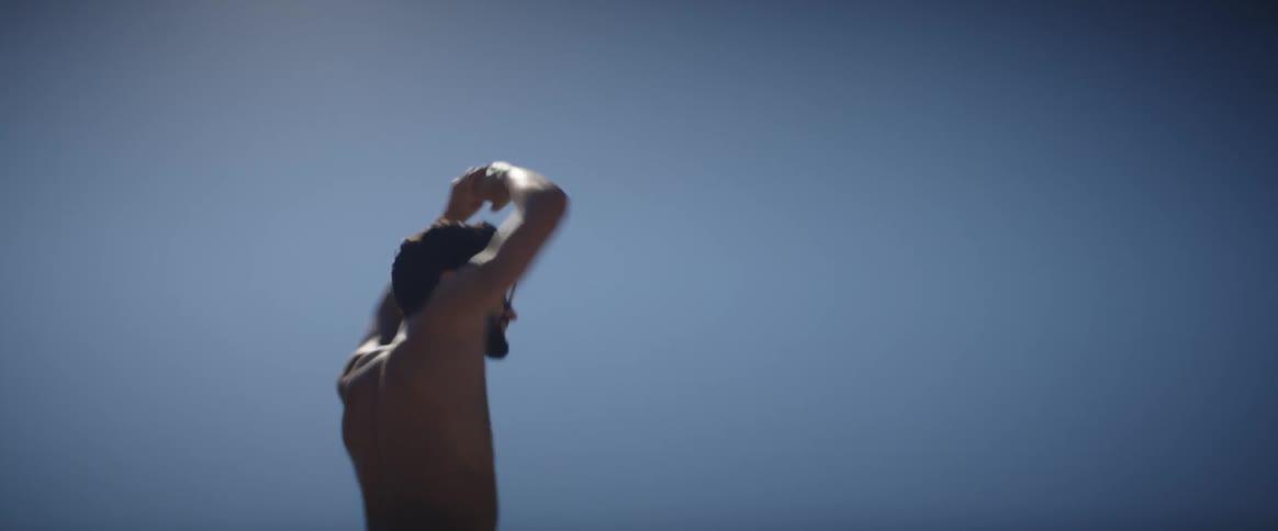 A portrait of a shirtless man dancing with his hands above his head