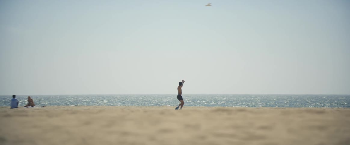 Shirtless man dancing near a beach at midday
