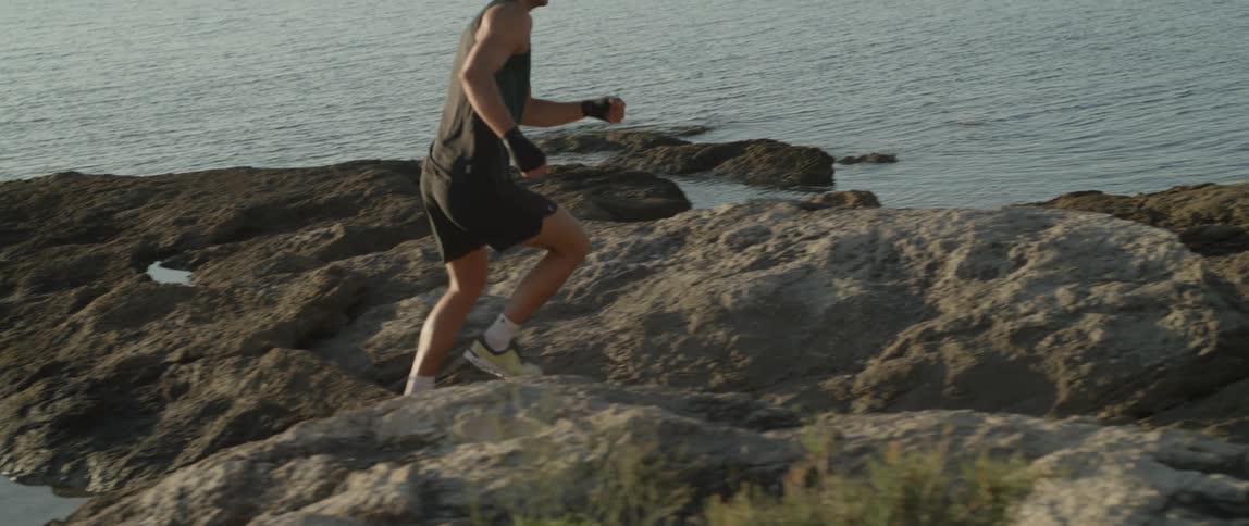 A man is running and jumping over the rocks on the shore