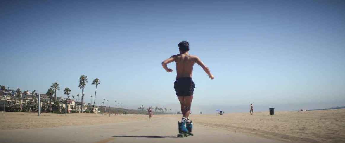 Young man running and dancing with roller skates on the beachside sidewalk during the summer
