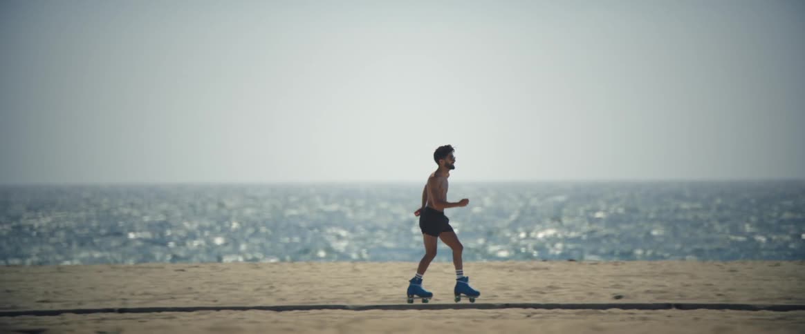 A man running and dancing with roller skates on the beachside sidewalk during the summer