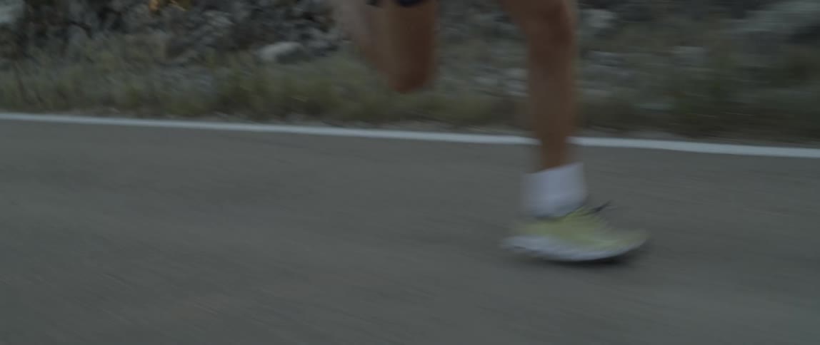 A man wearing running shoes sprints along a remote road