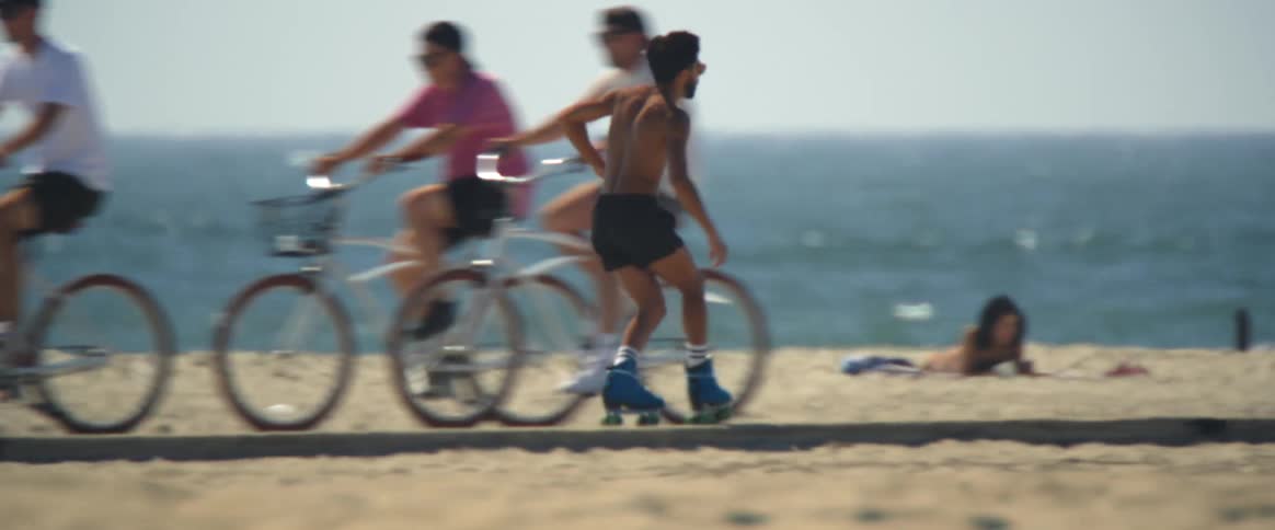 A man roller skating on the beachside sidewalk and dancing simultaneously