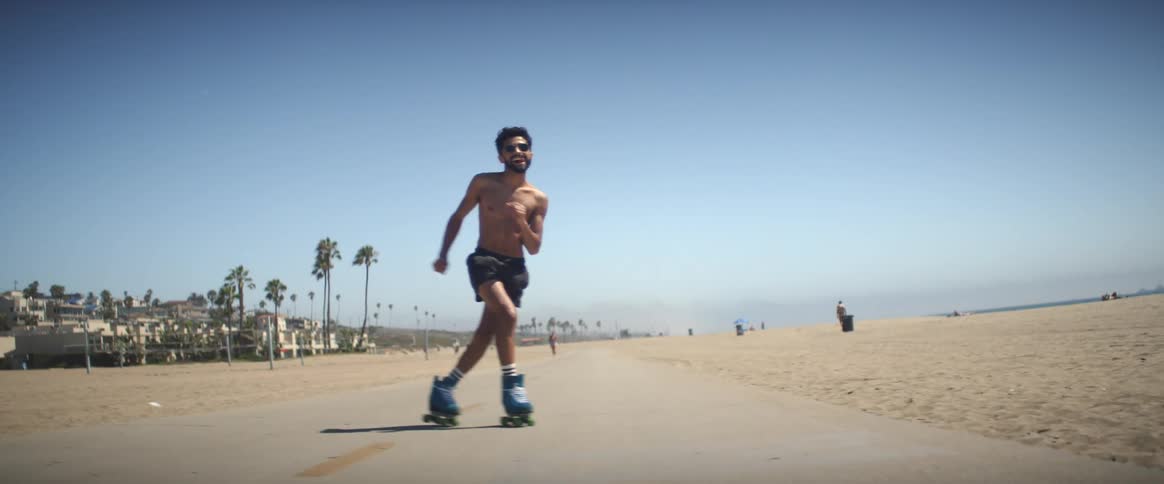 Um homem andando de patins rollers e danando na calada da praia