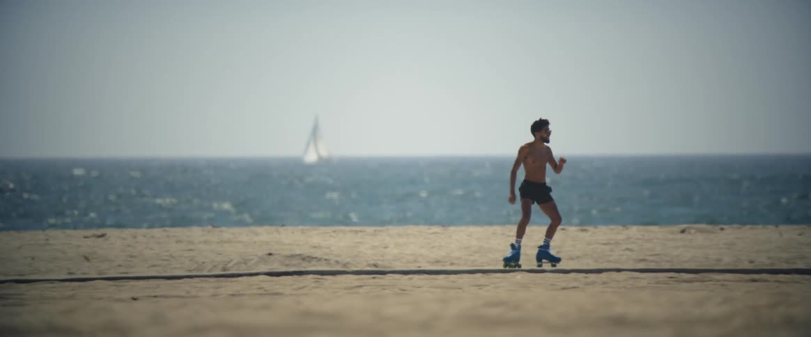 A man dancing with roller skates on a beachside sidewalk