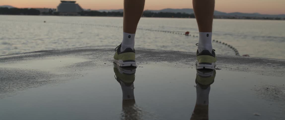 The legs of a person walking on a dock in sports sneakers at dawn