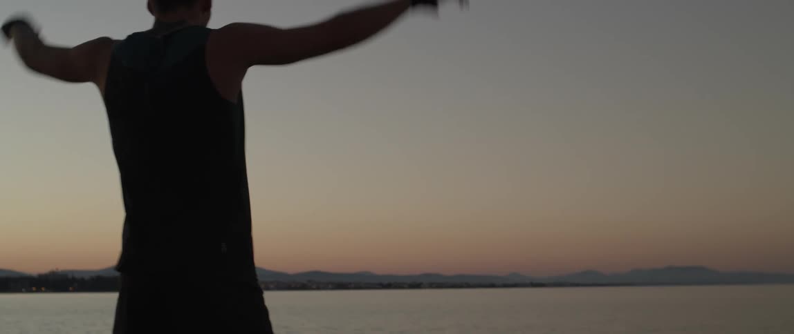 A man stretching his body facing the sea during a sunrise with his back to the viewer