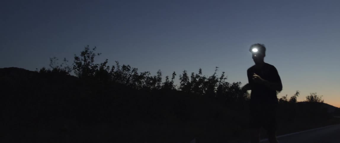 A man running with a headlamp on at dawn