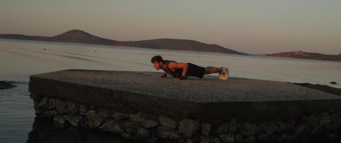 Strong young man does pushups next to the beach at sunset