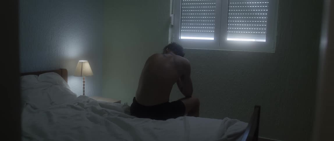 A man is sitting on the bed in his underwear in the bedroom