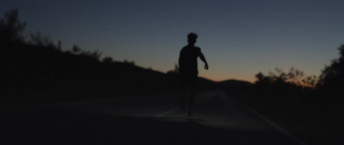 Silhouette of a man running on a road in the desert at nightfall