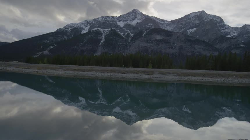 A still mountain lake reflecting the snow-capped mountains and cloudy sky