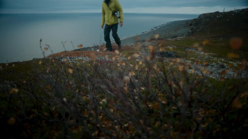 Photographer walks up slope from beach while carrying a camera