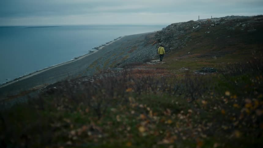 A man wearing a yellow coat walks on the hill near the beach