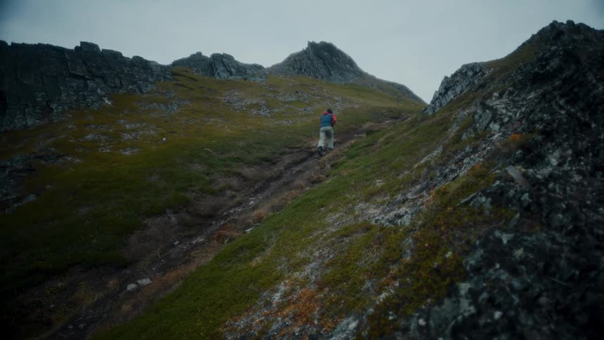 Person wearing coat walks up steep slope on cloudy day