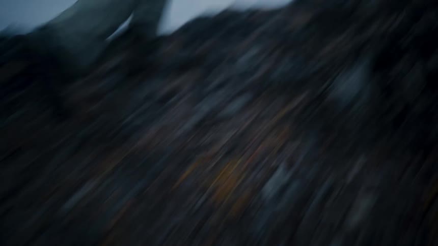Male camera runs up slope overlooking coast carrying a photographer