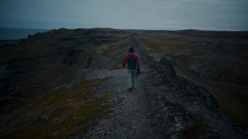 A man walking with his camera on a mountain next to the sea