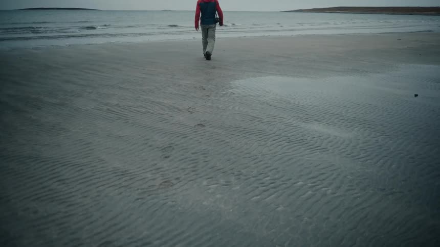 A man walking along the beach and taking photos with his camera