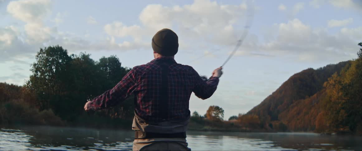 A man standing in a river with his back to the camera attempting to fish