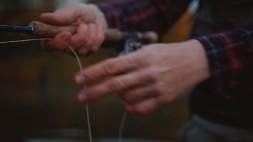 An adult holds a fly fishing reel with one hand and pulls the fishing line with the other