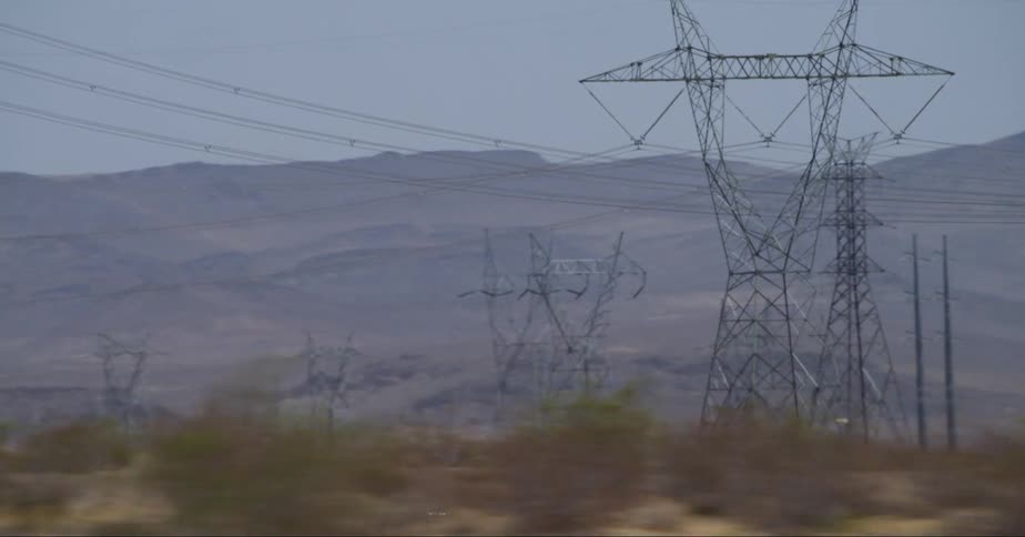 Electricity transmission towers in an outdoor setting with a mountain range in the background