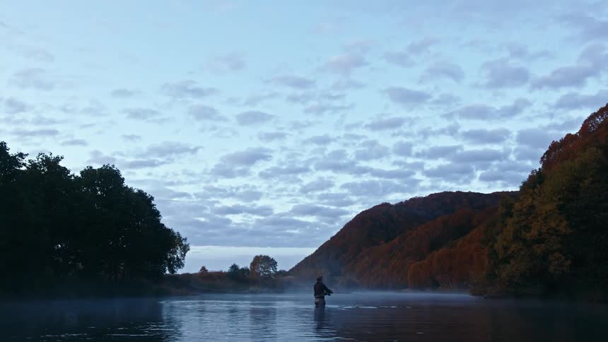 A man is fishing in the middle of a forest lake