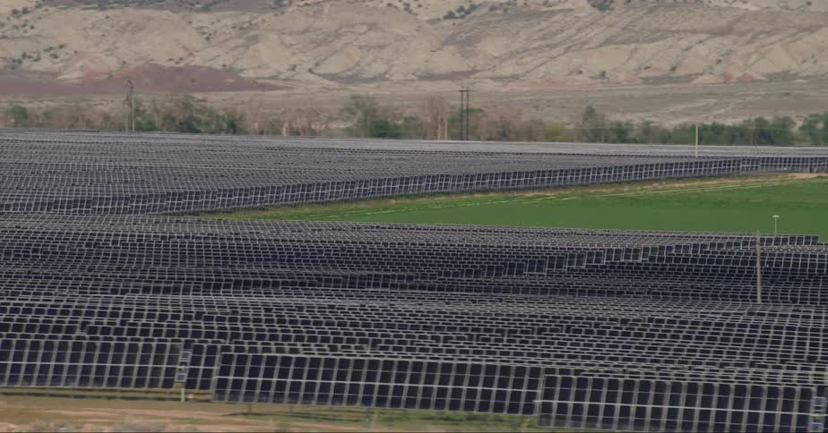 The solar panels on a solar farm are stretched across the land near mountains
