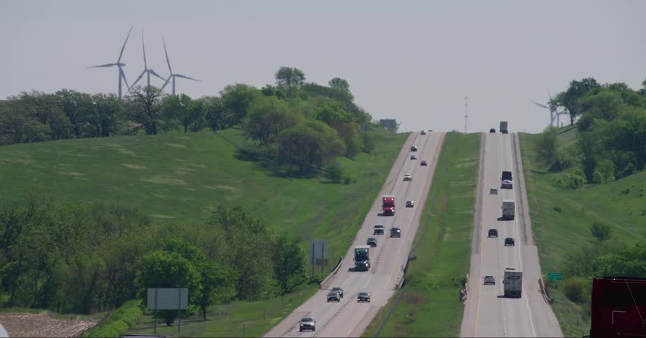 Traffic moves on roads over a hill as wind turbines spin on the roadsides