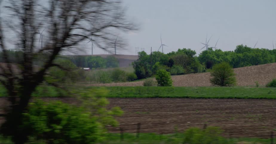 Flat grassland is being driven past with wind turbines in the background and cars passing by intermittently