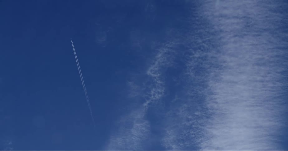 A jet airplane leaves a contrail as it flies near clouds in a deep blue sky