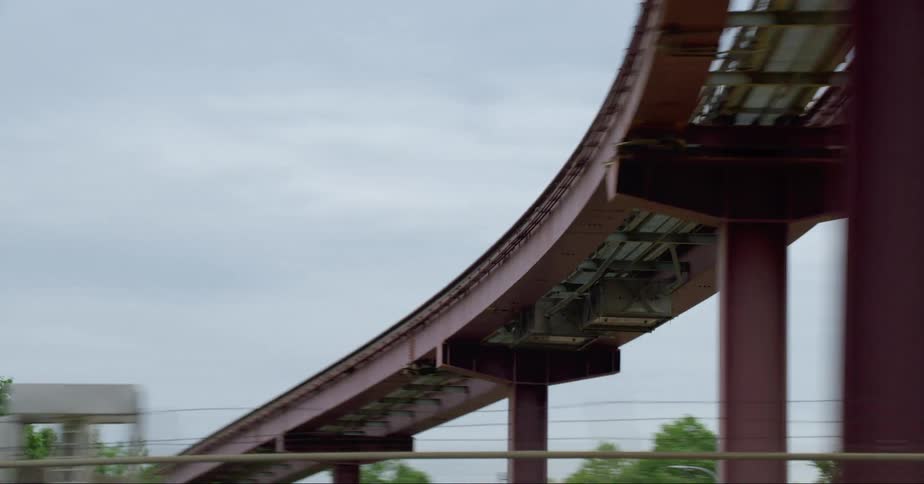 An overhead monorail is filmed from a moving car on a city street