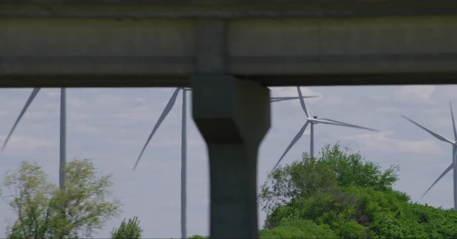 Wind turbines spin on a wind farm overlooking traffic on a busy road