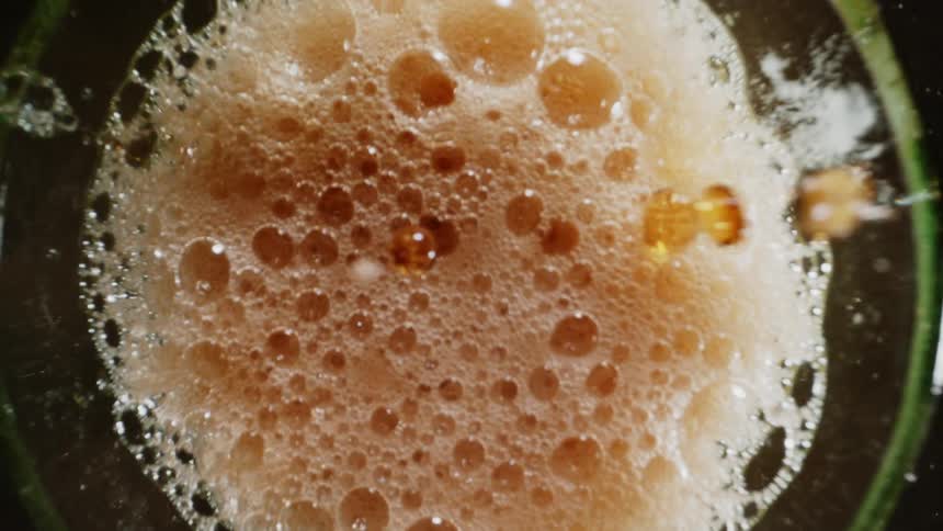 A glass of cola is being poured while magnifying the carbonation and falling drops