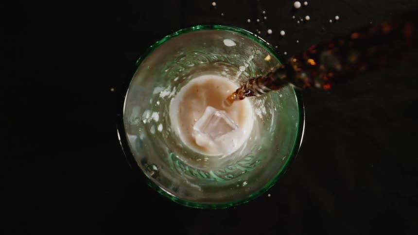 A drink being poured into a glass with ice and foam