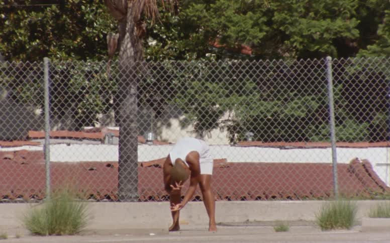 Woman with short hair white tank top and shorts dances in front of mesh fence