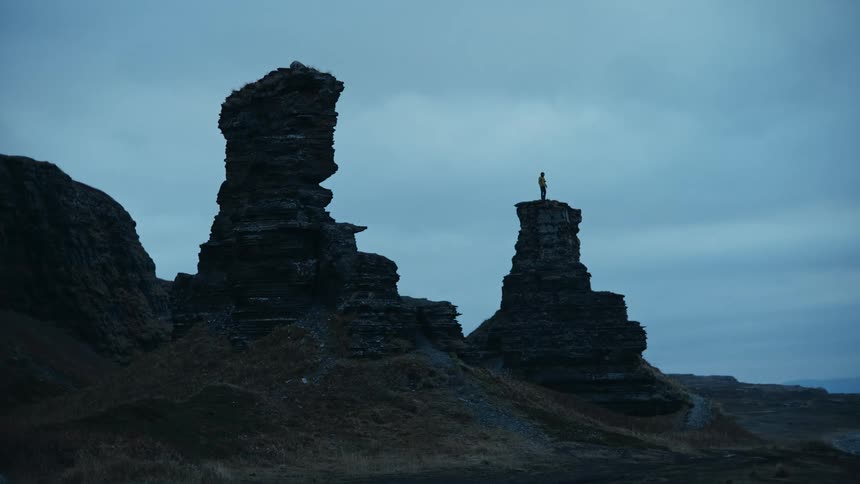A person stands on some rocky pillar outcroppings in the badlands at dusk