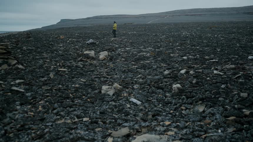 A man walking and taking photographs in a coastal environment with black rocks