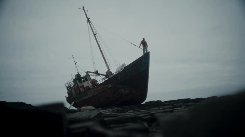 A ship anchored on the rocky coast of a sea with a person inside