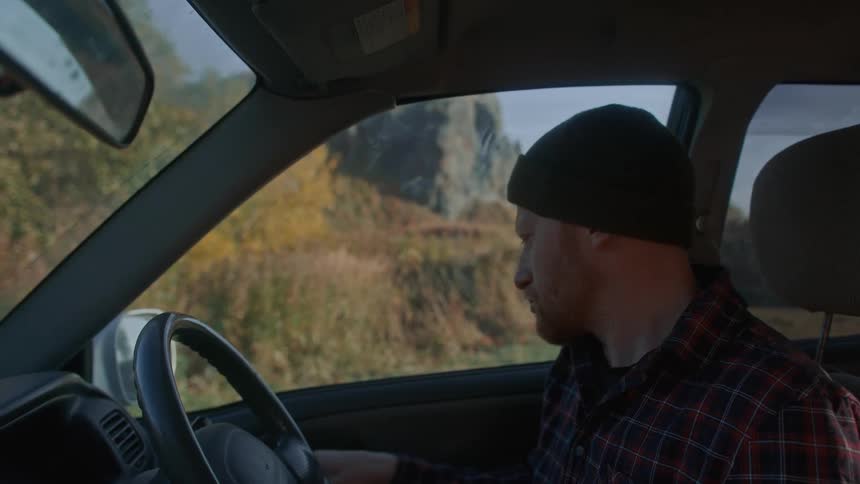 Man with beard black beanie and plaid shirt gets out of the car